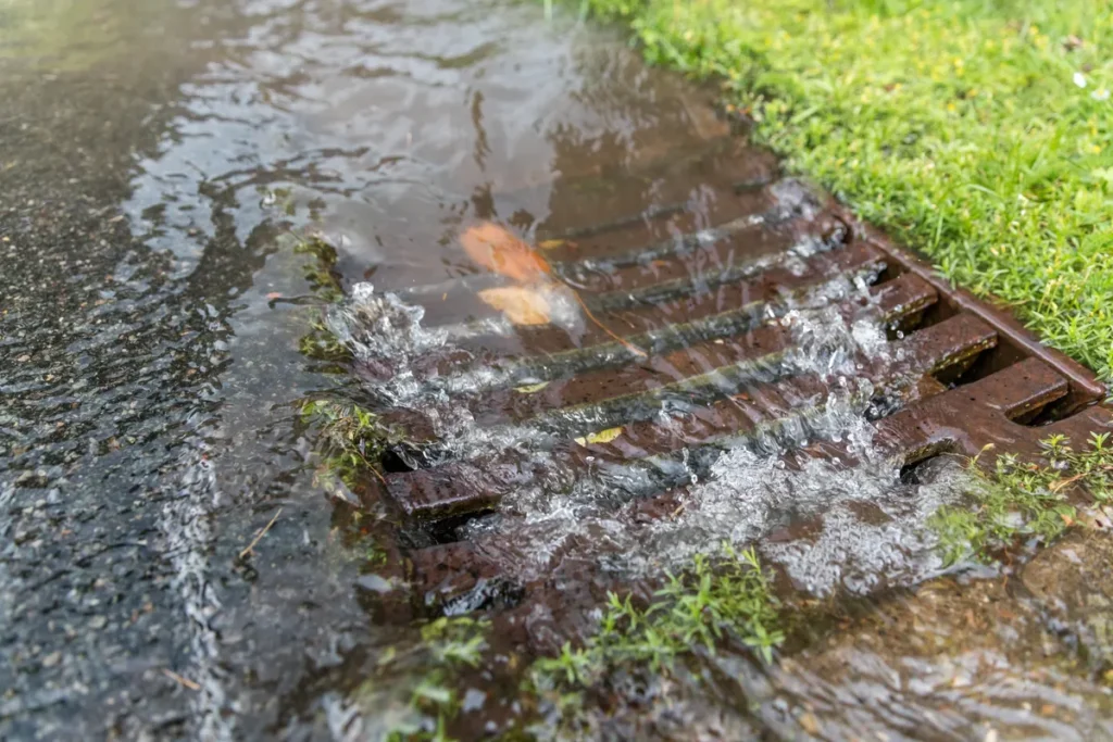 Storm water surging around an overwhelmed drain — Tolleson’s prewar core relies on aging sewer and storm laterals, and monsoon rain ponds against slab edges graded for the flood-irrigation era
