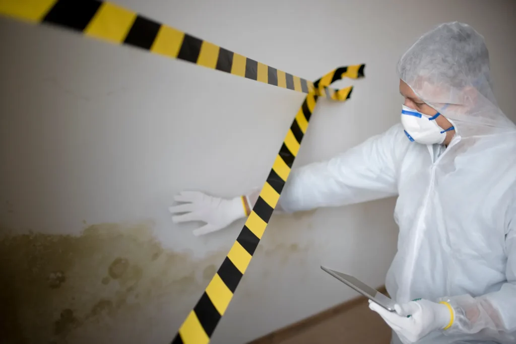 Remediation technician in a protective suit documenting mold on a wall behind a containment barrier, the controlled setup professional mold remediation in Tucson uses